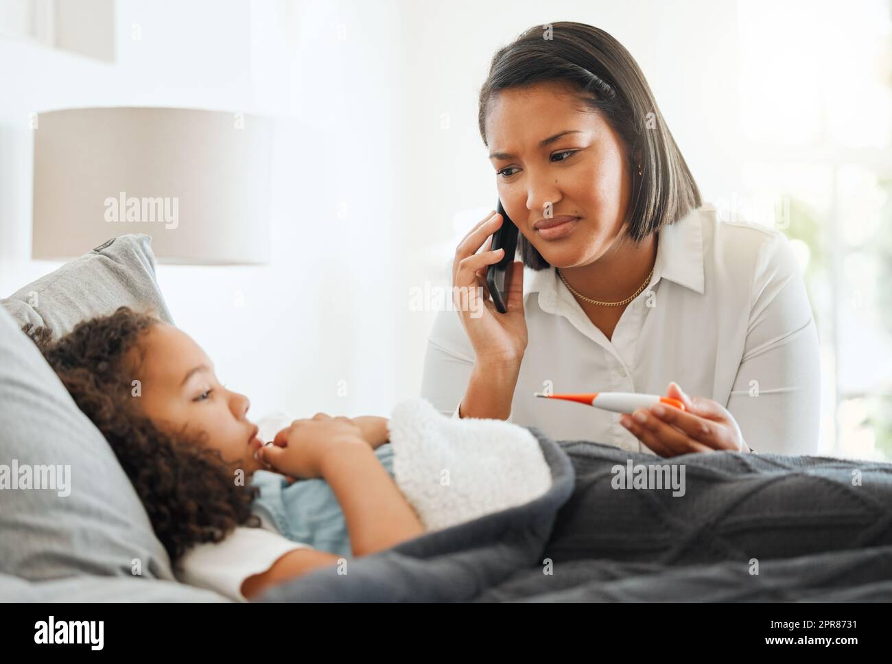 Theres niente di peggio che vedere la vostra bambina così ammalata. Una giovane madre al telefono mentre si prende cura della sua figlia ammalata a casa. Foto Stock