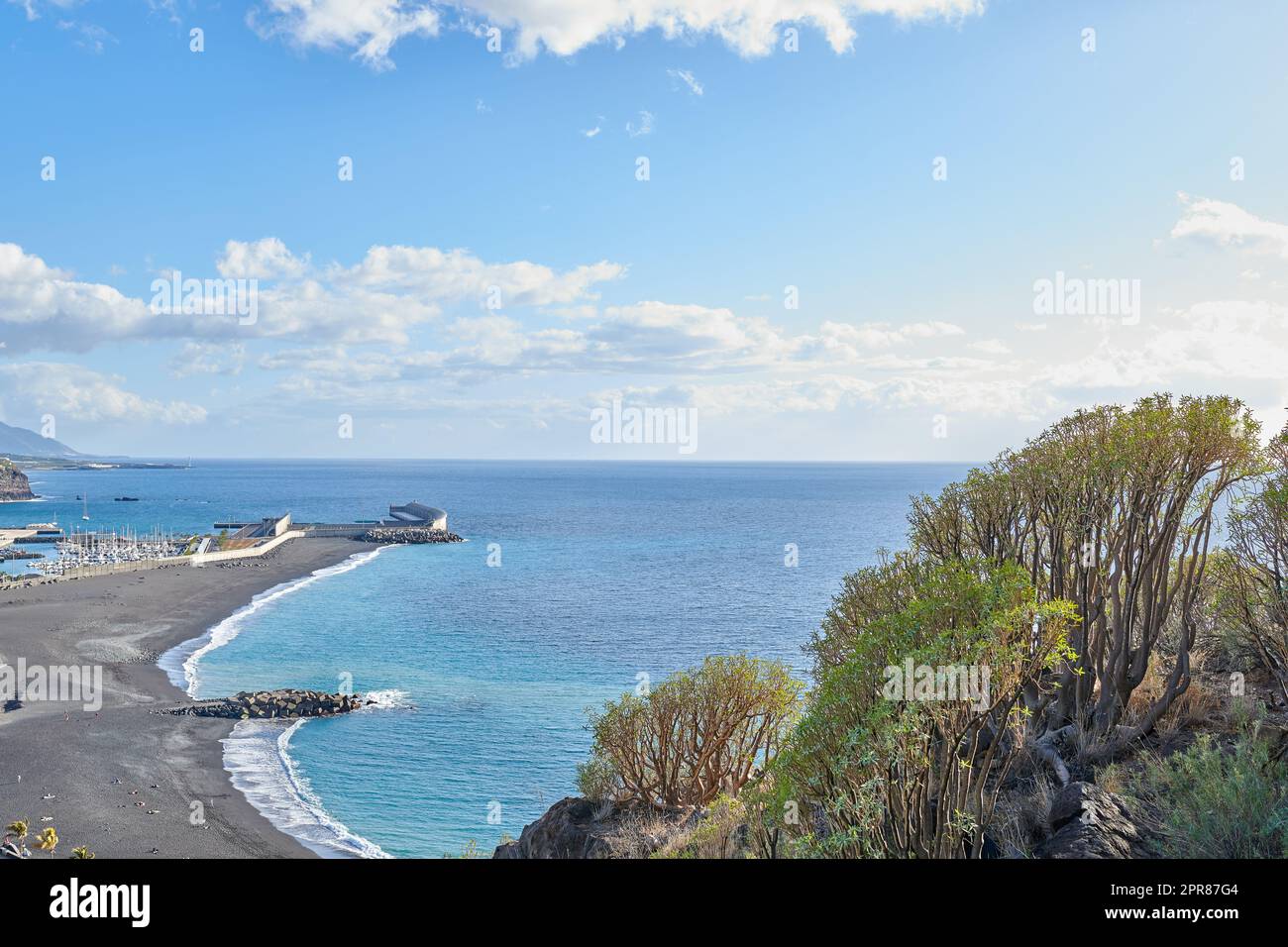 Litorale panoramico e paesaggio marino della città costiera turistica di Puerto de Tazacorte a la Palma, in Spagna durante l'estate. Vista panoramica di un mare con una spiaggia di sabbia nera, un cielo blu con nuvole e spazio per copiare. Foto Stock