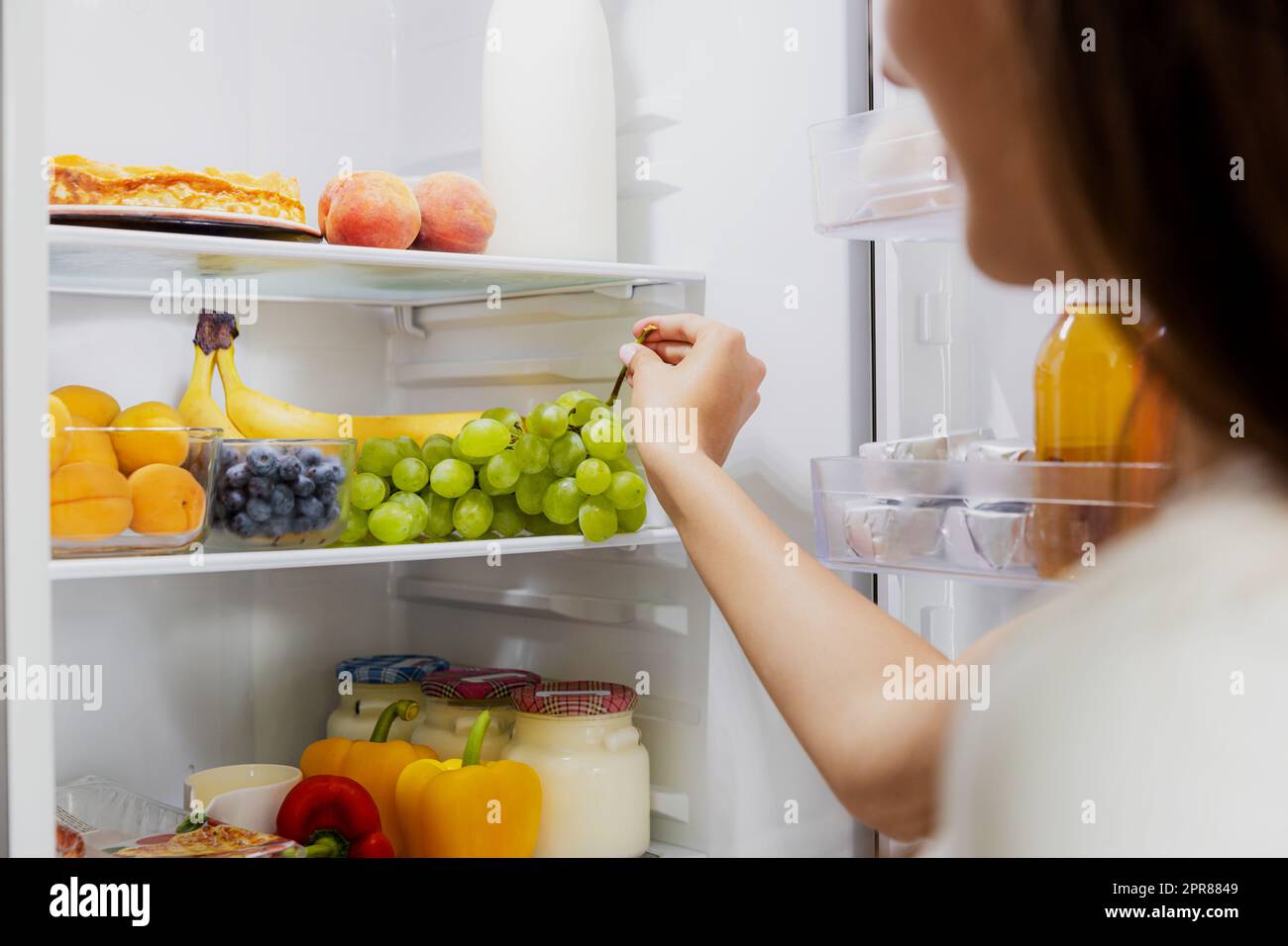 Una donna che prende o raccoglie un mazzo di uva dal frigorifero o dal frigorifero aperto Foto Stock