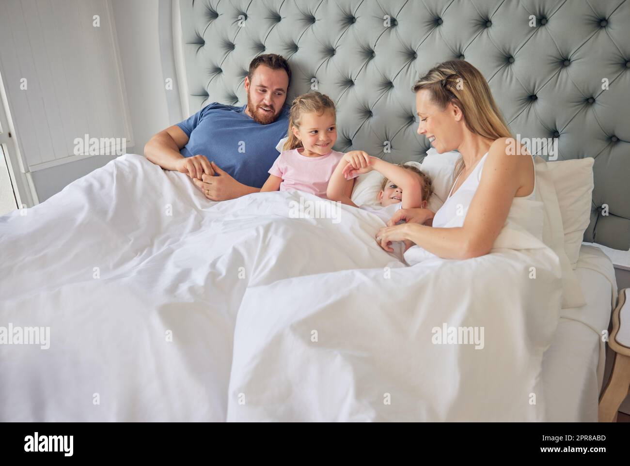 Felice famiglia caucasica sdraiata a letto con due figlie. Due bambine che sembravano felici dopo essersi svegliate la mattina nel letto dei genitori. I bambini si rilassano a letto con mamma e papà Foto Stock