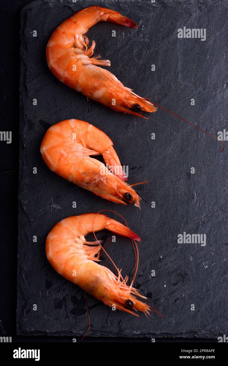 Vista dall'alto di gamberetti freschi sulla pietra nero ardesia con copyspace. Frutti di mare ingredienti preparazione. Foto Stock