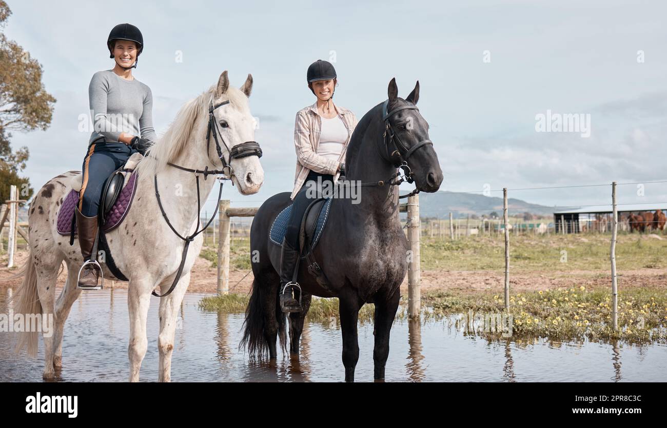 Trotting lungo. Sparo a tutta lunghezza di due giovani donne attraenti che cavalcano i cavalli all'aperto in un ranch. Foto Stock