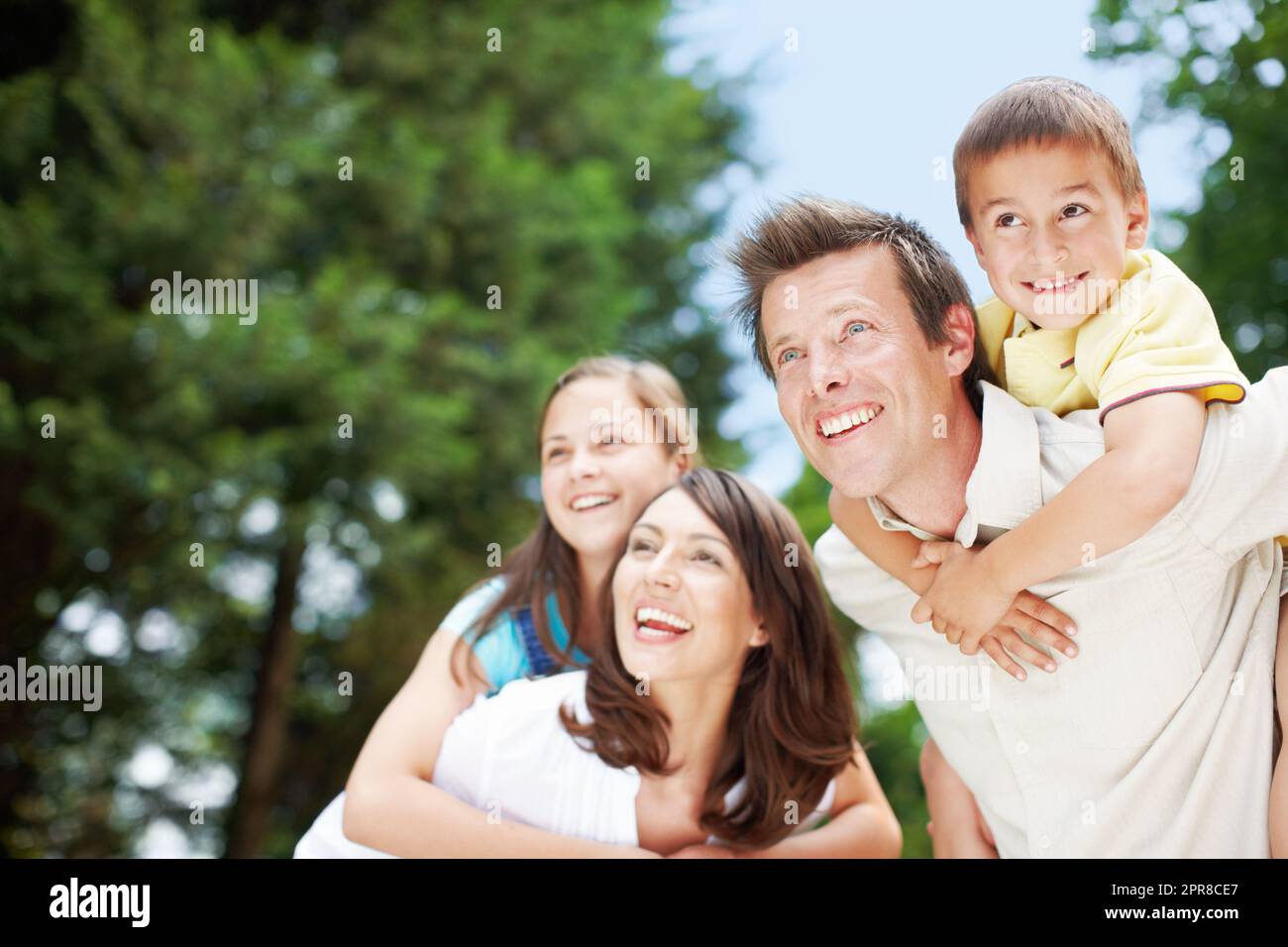 Una famiglia meravigliosa che si gode una giornata fuori insieme. Vista bassa di una madre e di un padre felici e devoti che portano i loro figli sulle spalle - CopySpace. Foto Stock
