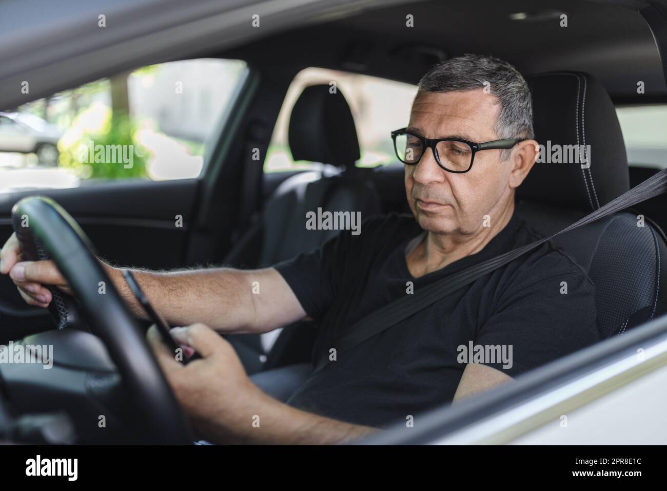 Senior di 70 anni alla guida di un'auto e usando il suo cellulare Foto Stock