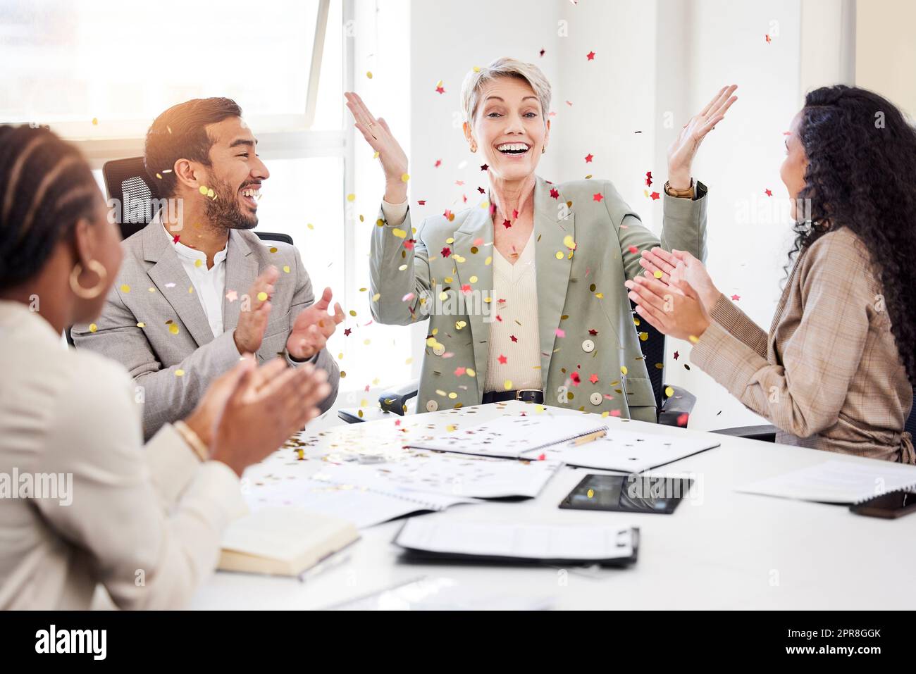 Questo merita qualche celebrazione: Una donna d'affari matura seduta con i suoi colleghi e gettando dei dolci per celebrare un successo durante un incontro. Foto Stock