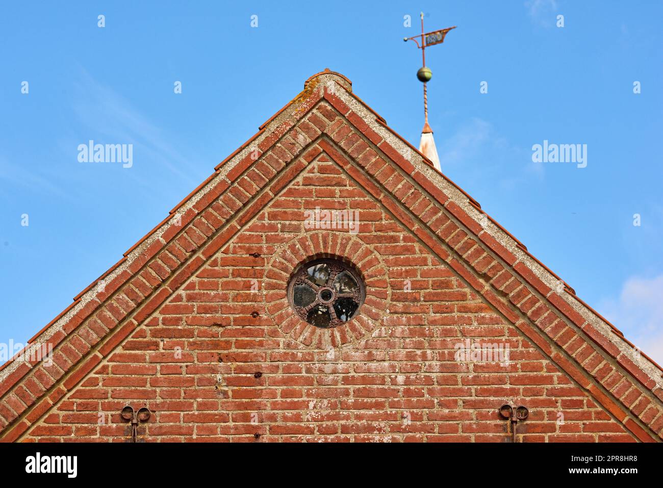 Vista di una finestra rotonda su un vecchio muro di mattoni rossi di una casa o di una casa. Vetro con struttura in metallo su edificio storico della chiesa. Design architettonico e dettagli su una struttura cittadina all'esterno con spazio per la copia Foto Stock