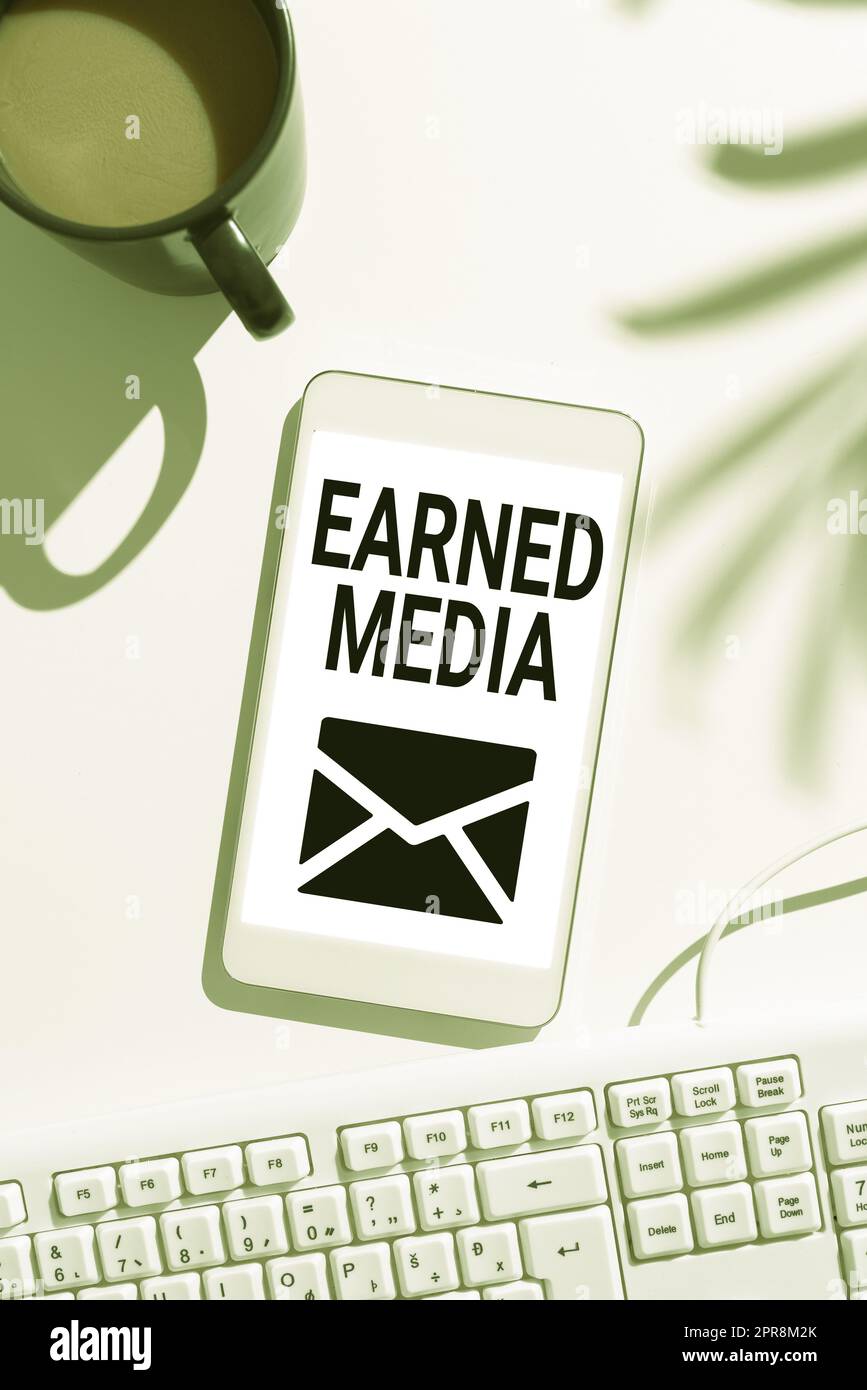 Scrittura visualizzazione di testo media guadagnati. Pubblicità fotografica concettuale ottenuta grazie agli sforzi promozionali realizzati dallo schermo multimediale del telefono cellulare con messaggio importante sulla scrivania con caffè e tastiera Foto Stock