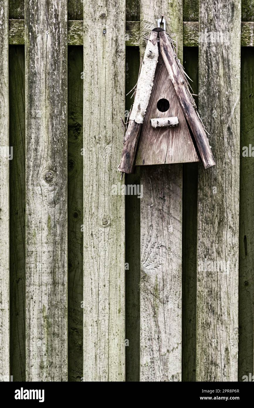 Vecchio alimentatore di uccelli in legno e rustico appeso a una recinzione in un giardino sul retro. Primo piano di una casa per uccelli d'epoca su un muro esterno. Recinti costruiti per gli uccelli nel loro ambiente naturale e habitat Foto Stock