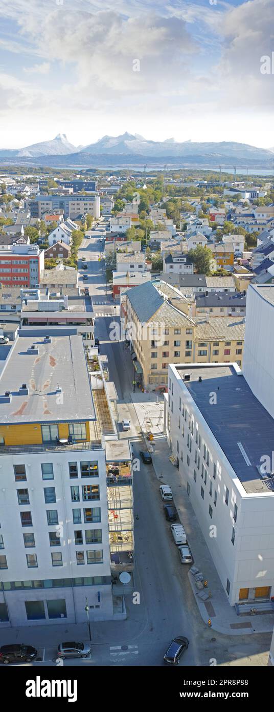 Vista sopra le strade urbane della città nella popolare destinazione di viaggio d'oltremare di Bodo, Norvegia. Centro cittadino trafficato e infrastruttura urbana di architettura edile con montagne panoramiche sullo sfondo Foto Stock