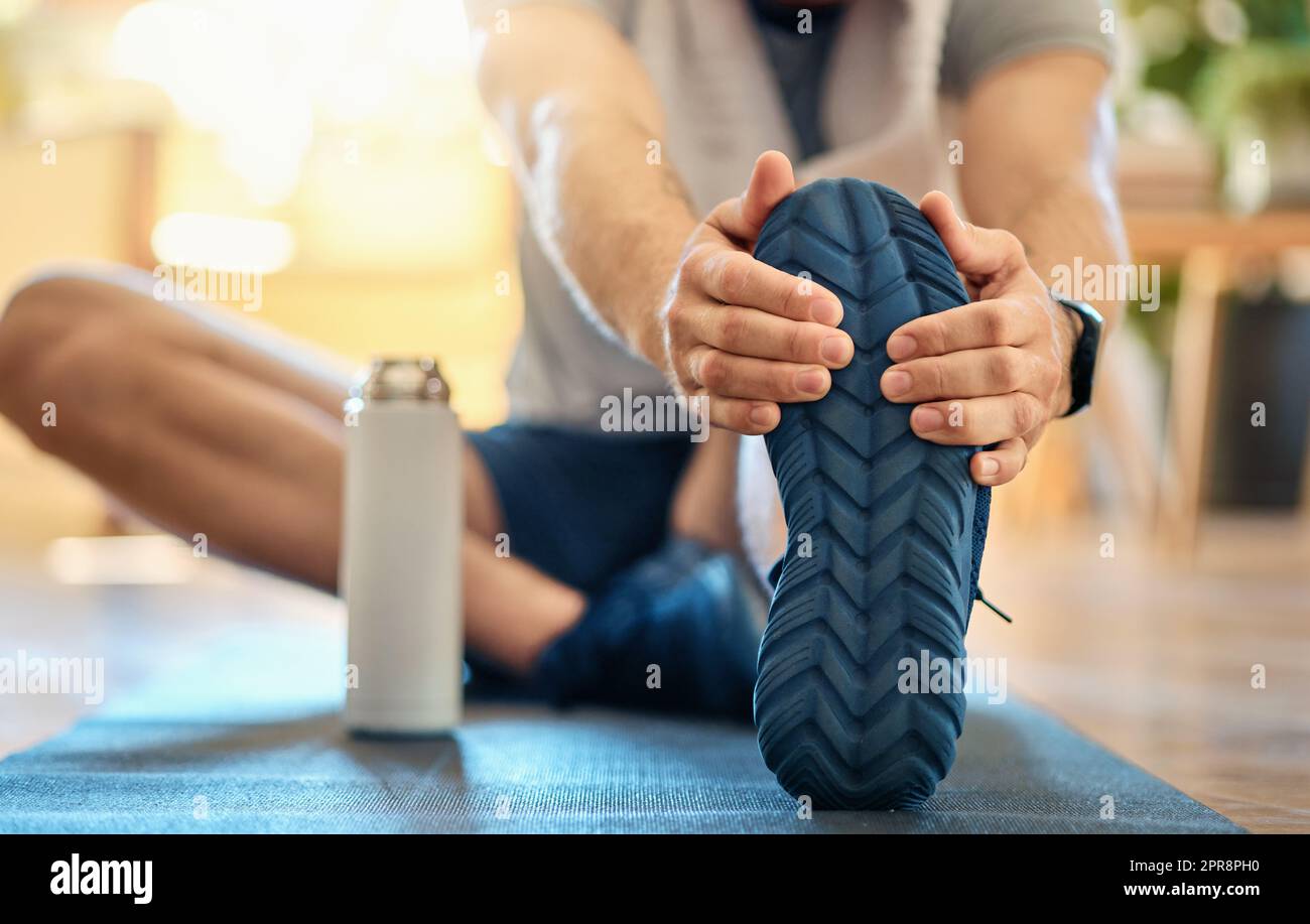 Primo piano di un uomo caucasico attivo che tocca i piedi e allunga le  gambe per riscaldare per evitare lesioni durante l'esercizio fisico a casa.  Suola inferiore di scarpe di ragazzo che