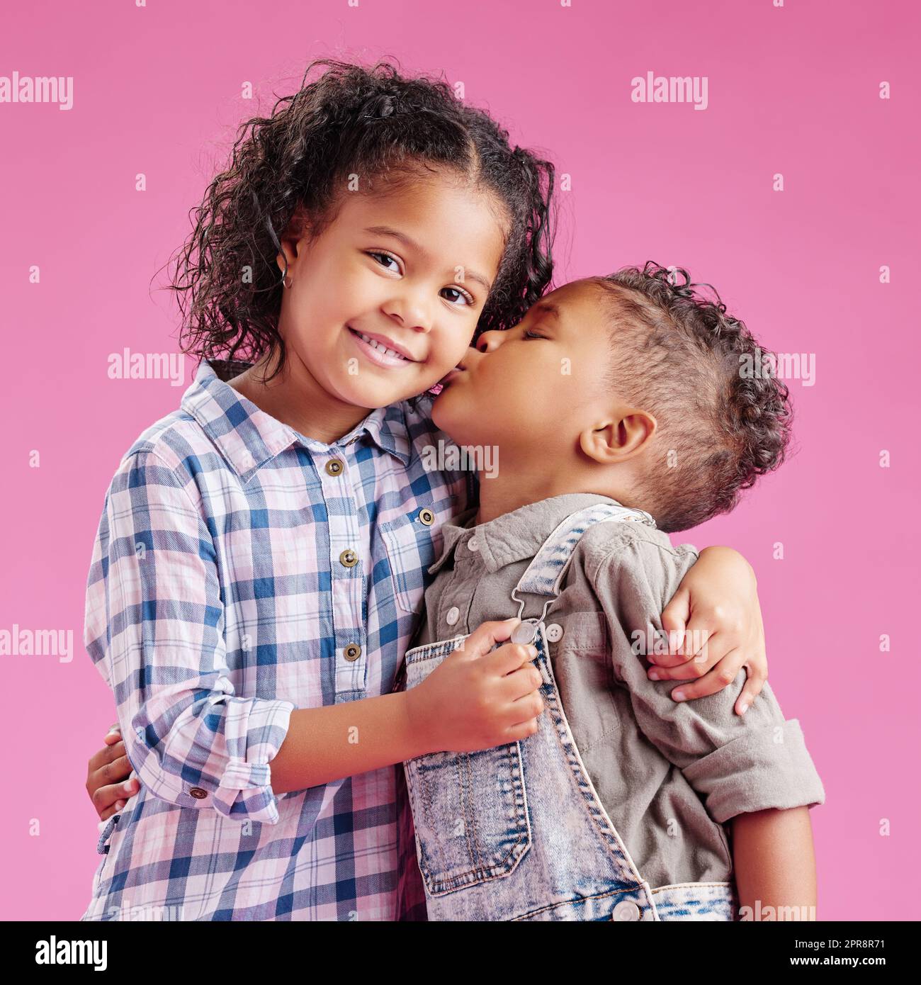 Due bambini solo in posa ed essere affezionati su uno sfondo rosa copyspace. Fratelli afroamericani di razza mista che si baciano mentre si legano in uno studio Foto Stock