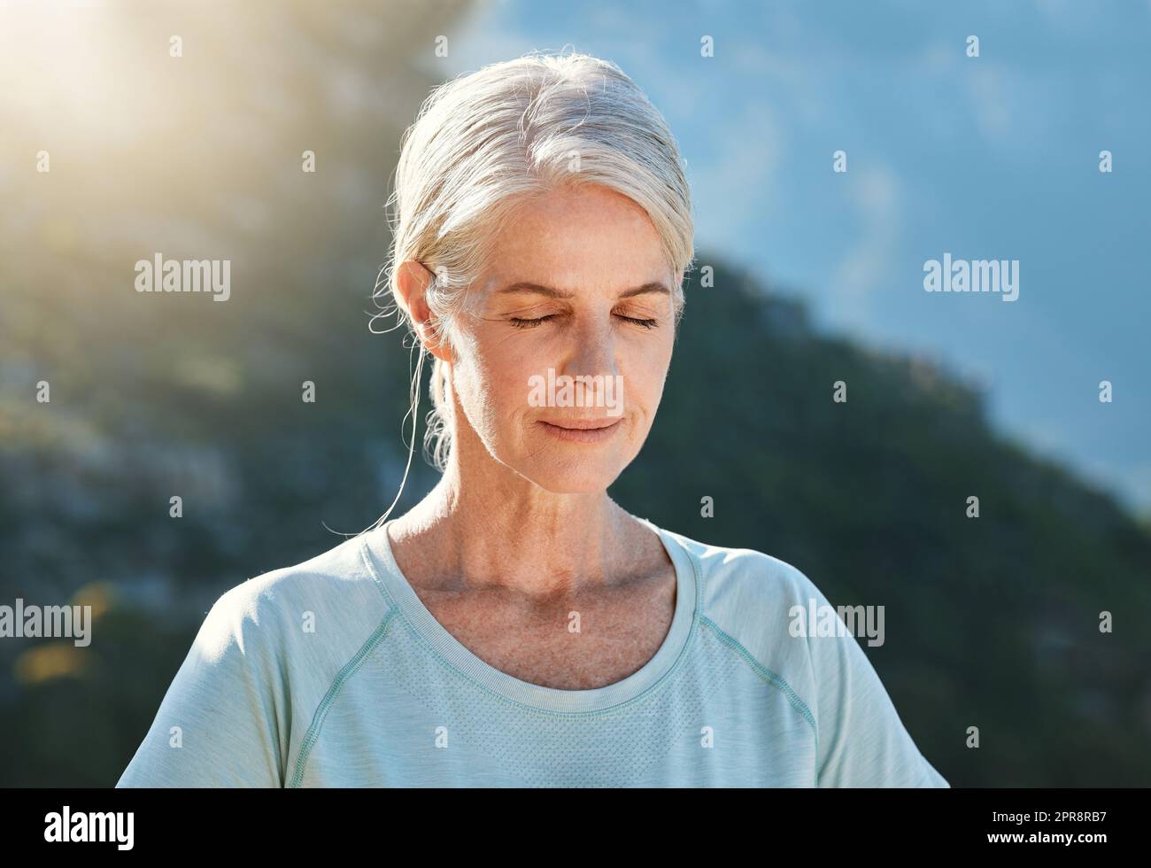 Donna anziana con capelli grigi in piedi all'esterno con gli occhi chiusi e respirando profondamente, meditando nella natura. Trovare pace interiore, equilibrio e vivere sano Foto Stock