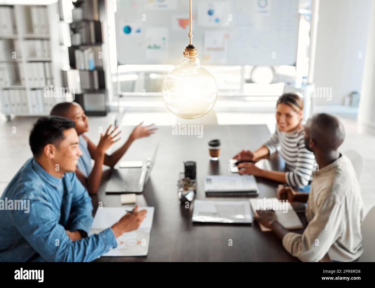Lampadina luminosa appesa al tetto mentre un gruppo di uomini d'affari si riunisce in un ufficio al lavoro. Bulbo rappresenta idee, idee, creatività e ispirazione. Colleghi che pianificano insieme Foto Stock