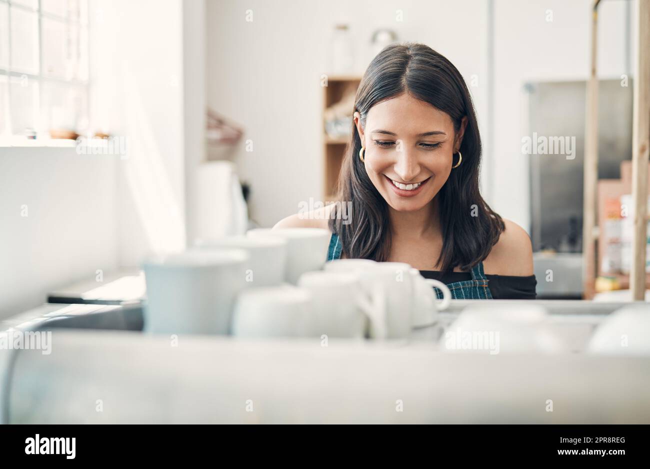 Una cameriera ispanica felice che usa una macchina per il caffè per preparare una bevanda calda in un caffè. Barista felice che prepara una bevanda calda per servire i clienti in una caffetteria Foto Stock