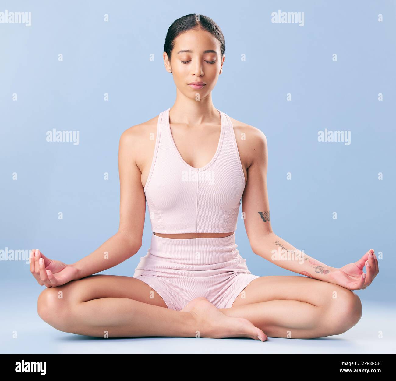 Atleta mista che medita e pratica yoga in studio su uno sfondo blu. Giovane donna ispanica che trova il suo centro, la pace interiore e l'equilibrio. Essere consapevole del suo viaggio verso Zen Foto Stock