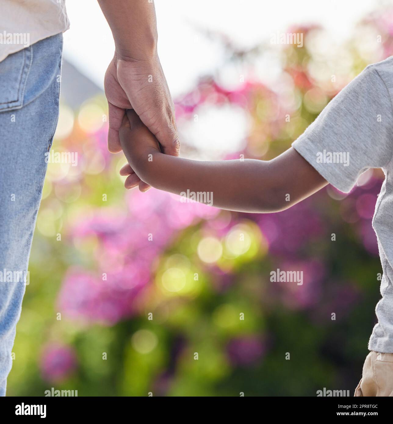 Primo piano del bambino che tiene i padri per mano con lo sfondo della natura. Famiglia afroamericana che si tiene per mano mostrando amore, sostegno e affetto. Un genitore dà una guida a un bambino e lo tiene al sicuro Foto Stock