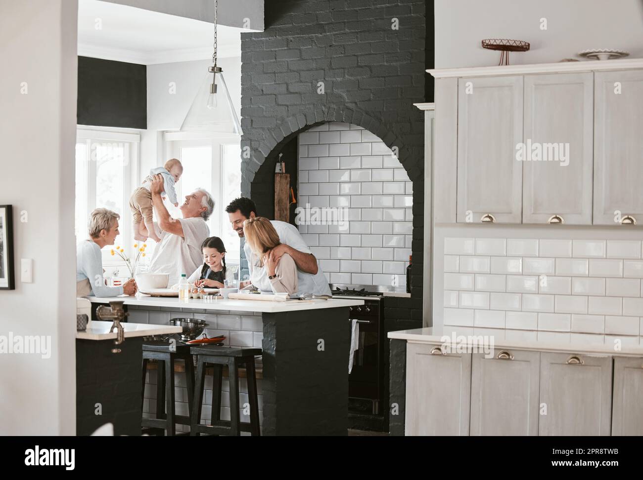 . Felice famiglia caucasica multi-generazione che prepara insieme e parla in cucina. Incollaggio prolungato in famiglia durante la miscelazione degli ingredienti per una torta. Una bambina che fa il forno con i suoi genitori e i suoi nonni. Foto Stock