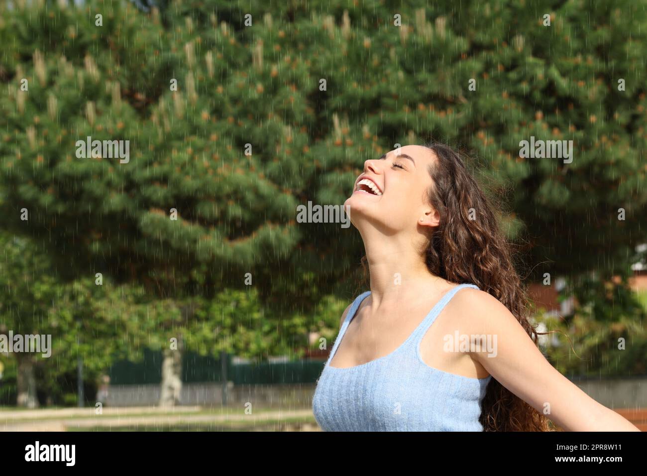 Donna felice che respira sotto la pioggia in un parco Foto Stock
