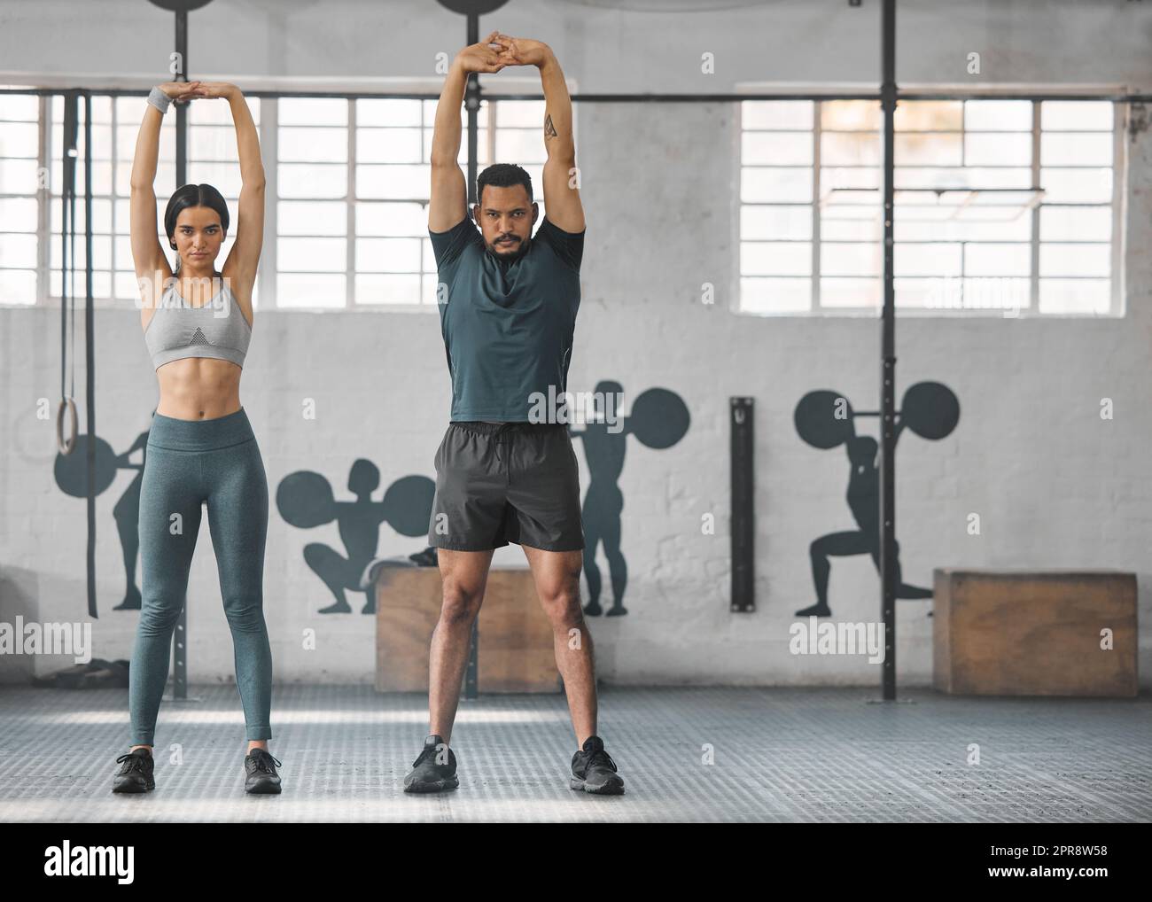 Fitness, coppia attiva e sana stretching, esercizio fisico o allenamento insieme all'interno della palestra. Due giovani allenatori in forma che fanno un esercizio di allenamento completo o una routine di riscaldamento diurno con spazio per le copie Foto Stock