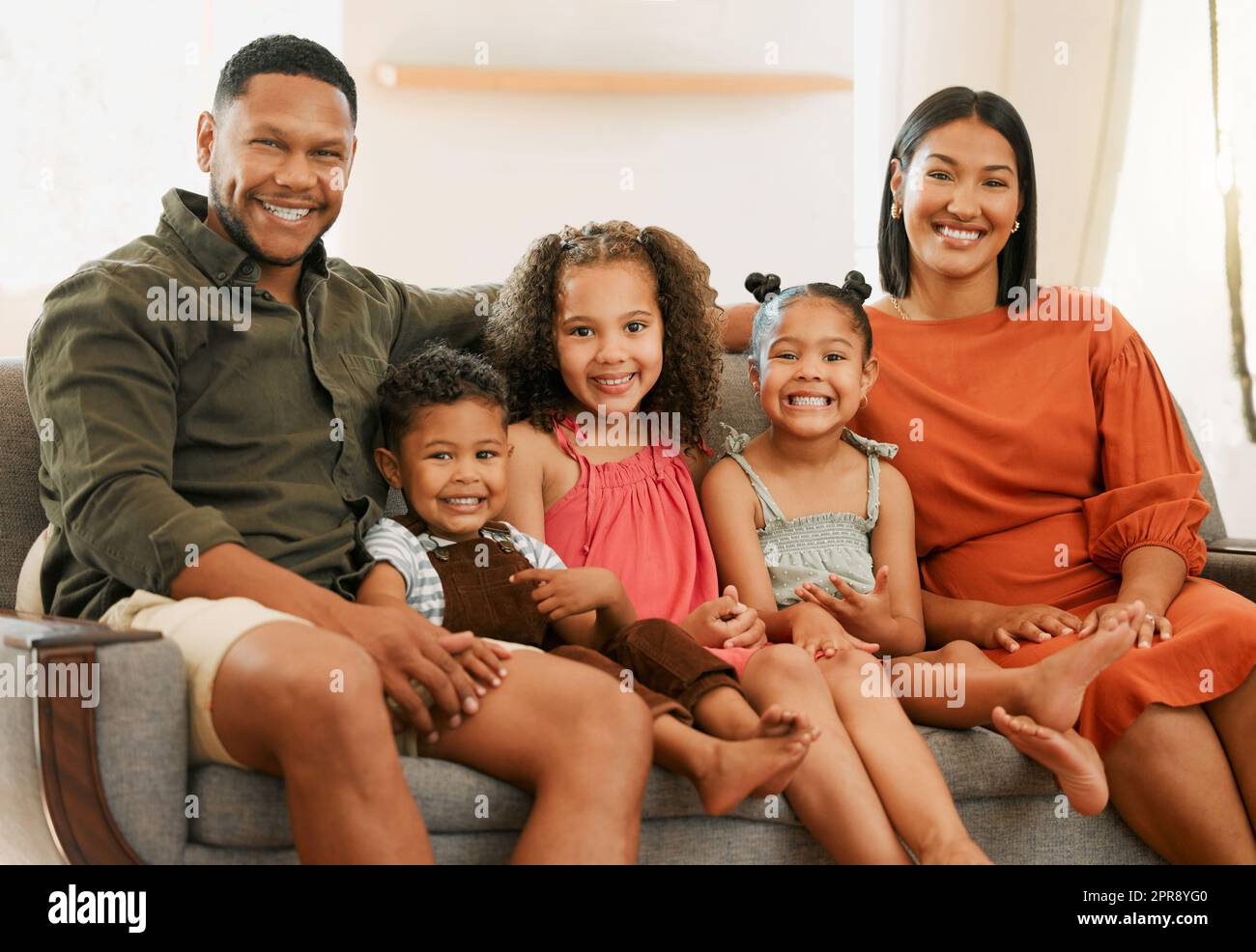 Ritratto di una famiglia mista di cinque persone che si rilassa sul divano a casa. Adoro la famiglia nera che si affettuosa sul divano. Giovani coppie che legano con i loro figli adottivi a casa Foto Stock