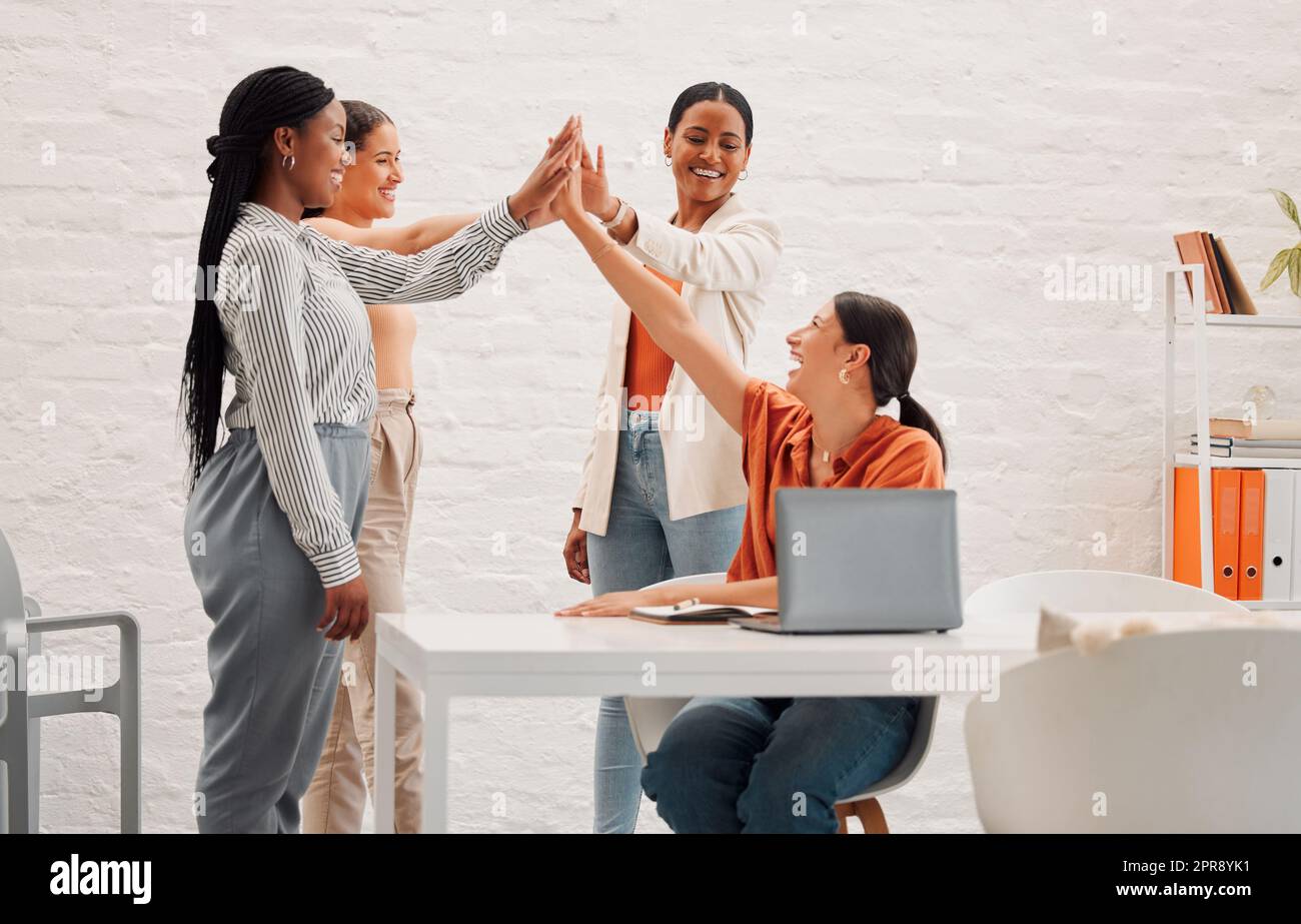 Quattro donne d'affari felici che si uniscono insieme in un ufficio al lavoro. Gruppo eterogeneo di uomini d'affari allegri che si danno a vicenda un massimo di cinque per il supporto Foto Stock
