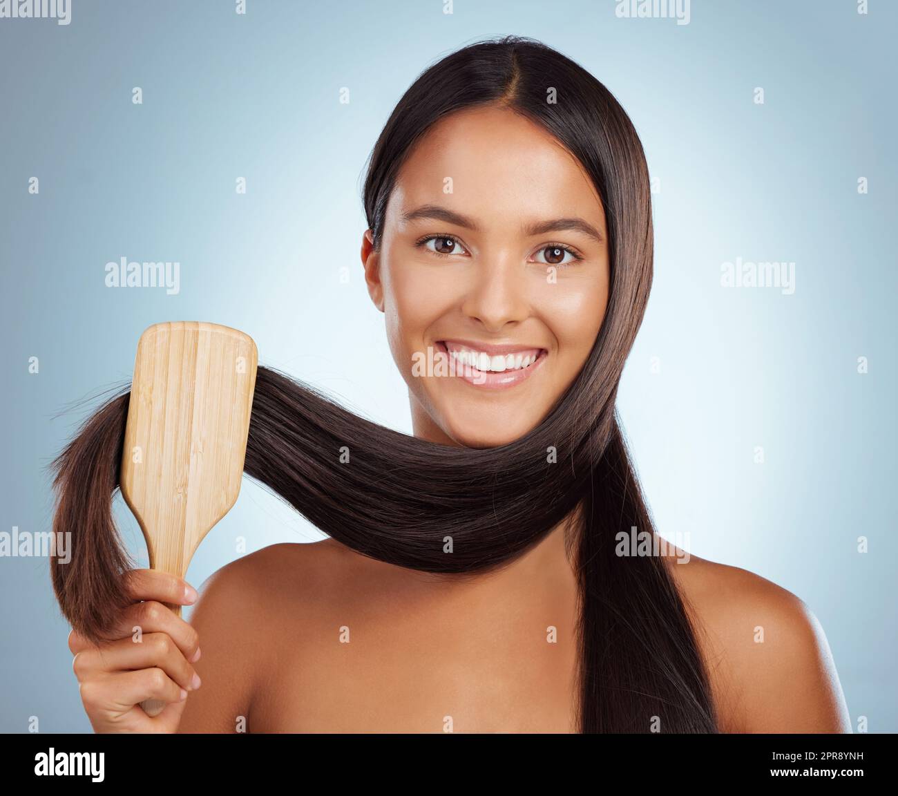 Ritratto di una bella giovane donna mista gara spazzolando i suoi capelli sani e forti su uno sfondo grigio studio. Femmina ispanica che grooming i suoi capelli Foto Stock