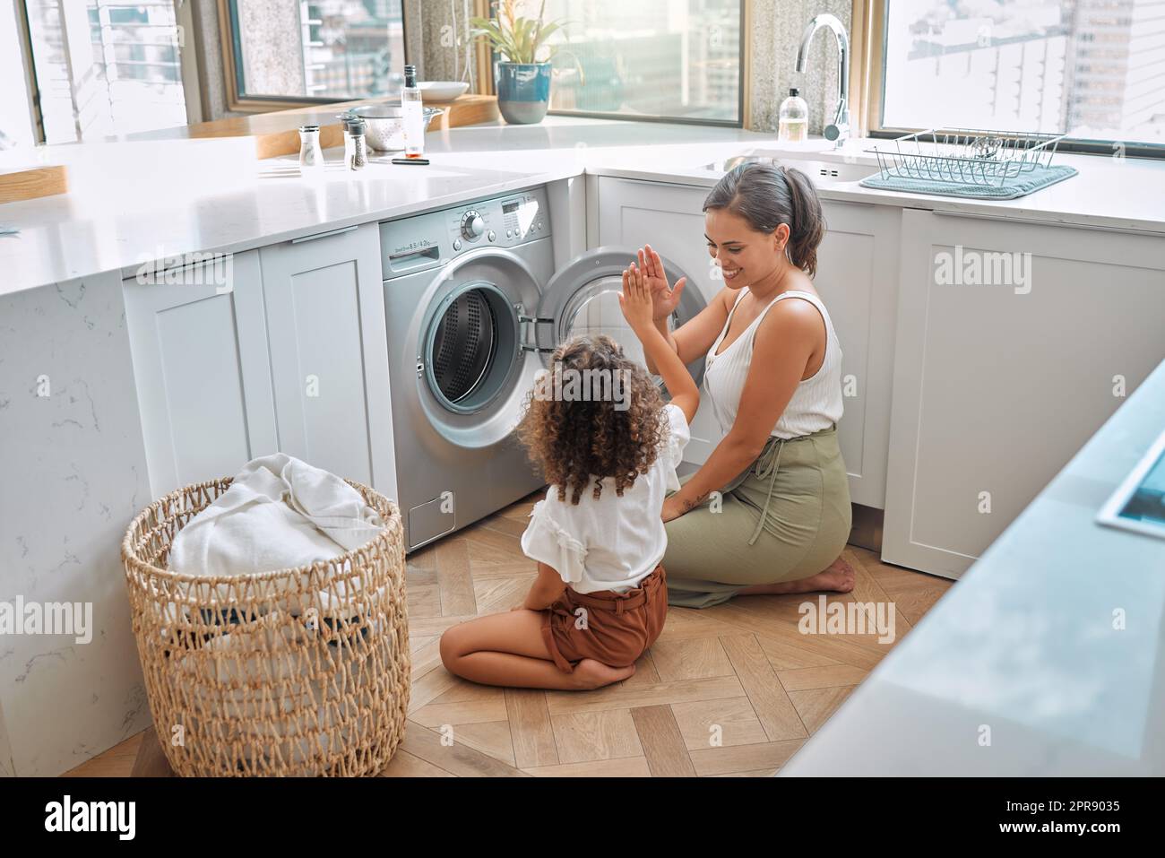 La giovane madre ispanica e sua figlia si danno cinque dollari dopo aver fatto il bucato a casa. Adorabile bambina che aiuta sua madre con le faccende domestiche Foto Stock