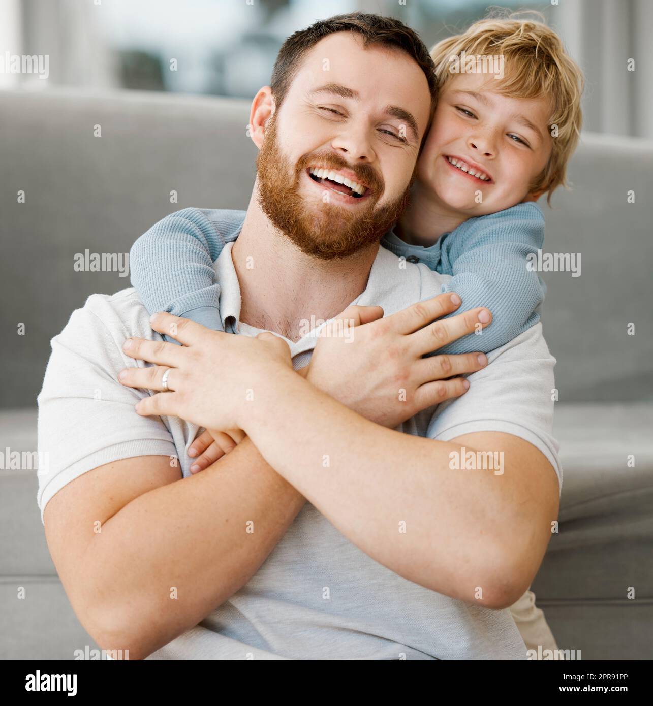 Carino piccolo ragazzo caucasico sorridente che abbraccia papà da dietro a casa. Spensierato e felice papà che riceve amore e affetto da un figlio giocoso. Un uomo che si sente speciale mentre si gode momenti speciali nella giornata del padre Foto Stock