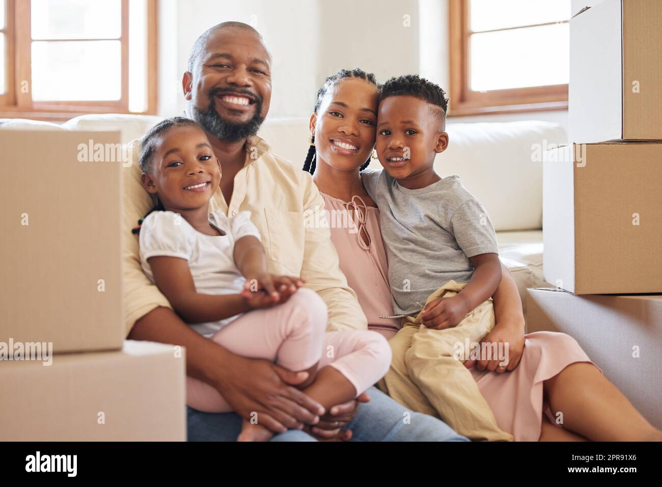 Felice famiglia afroamericana sorridente mentre sedeva sul pavimento in una nuova casa. Ritratto di una giovane felice coppia nera con due bambini che spostano le scatole nella loro nuova casa. Coppia nera che compra proprietà Foto Stock