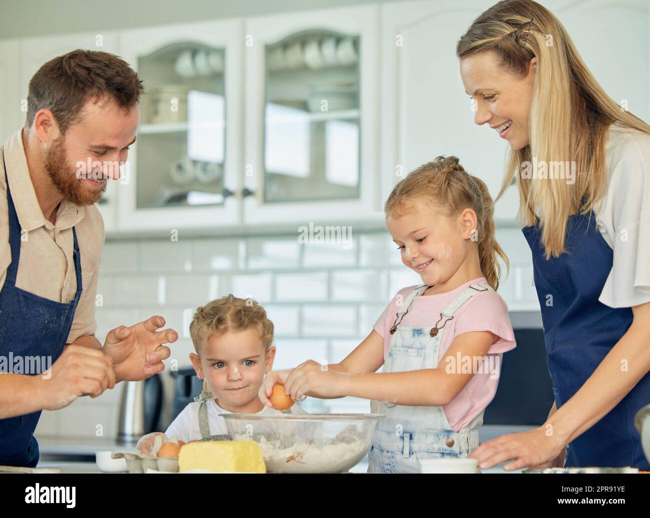 Una famiglia felice e amorevole sta facendo il forno insieme. Madre, padre e due figlie fanno biscotti e si divertono in cucina. Cibo fatto in casa e piccoli aiutanti che cucinano a casa. Foto Stock