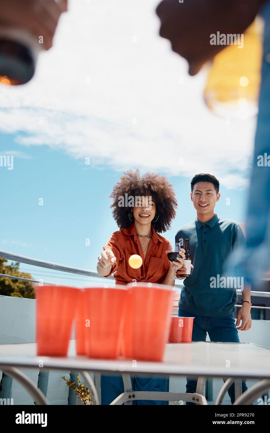 Felici giovani amici che giocano a beer pong insieme fuori. Amici diversi che lanciano una palla in tazze di birra. Giovane asiatico che si diverte e gioca a un gioco con il suo amico ispanico.sorridendo giovani amici Foto Stock