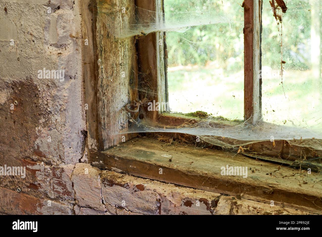 Vista interna di un'antica casa che ha bisogno di TLC. Una vecchia finestra con polvere e ragnatele in una casa abbandonata all'interno. Dettagli architettonici di un telaio del davanzale con texture rustiche danneggiate. Foto Stock
