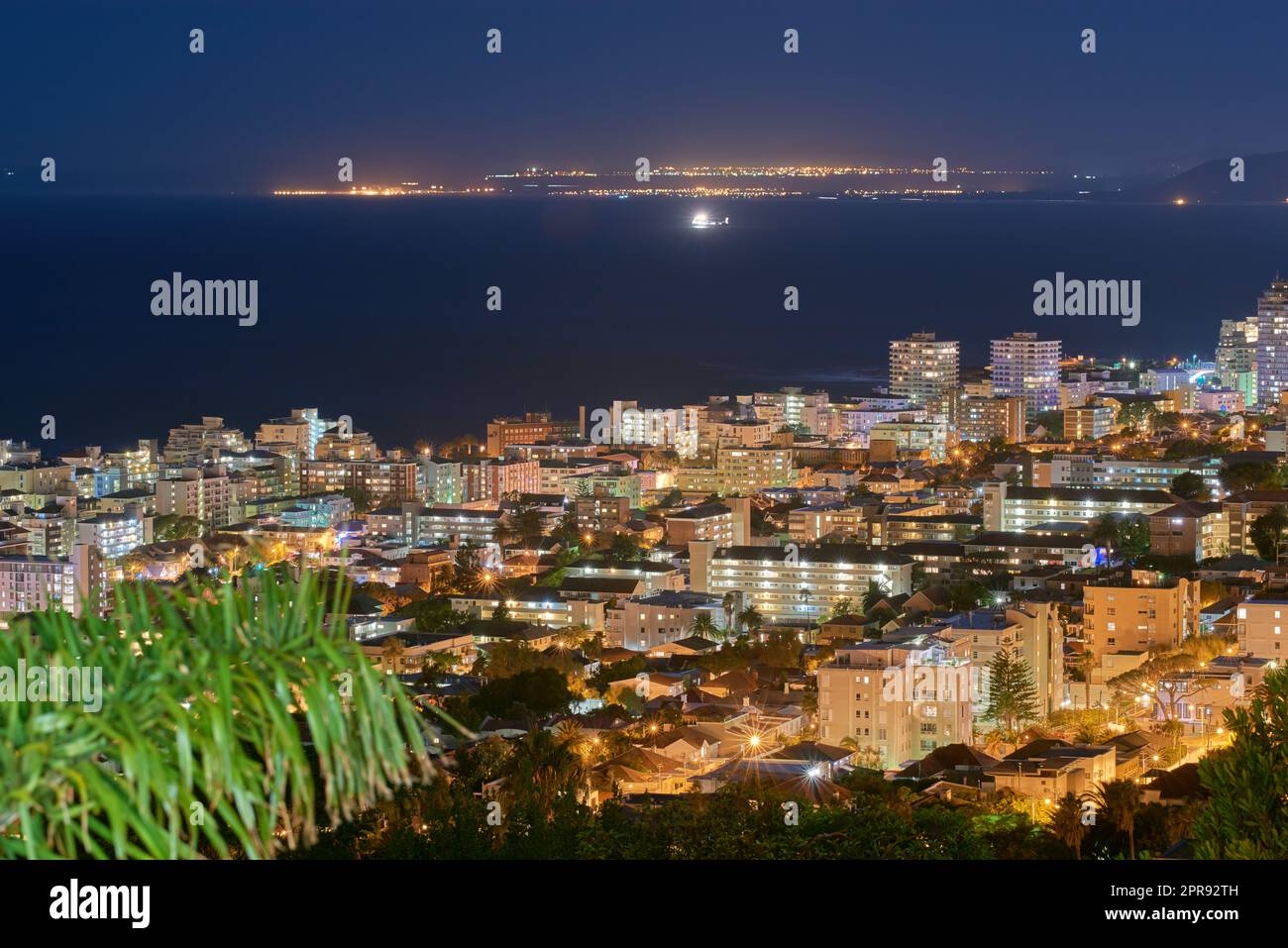 Le luci urbane della città si affacciano su un cielo di mezzanotte con spazio per le copie. Skyline con illuminazione colorata e l'oceano aperto all'orizzonte. Edifici architettonici moderni, hotel per vacanze in una città urbana Foto Stock