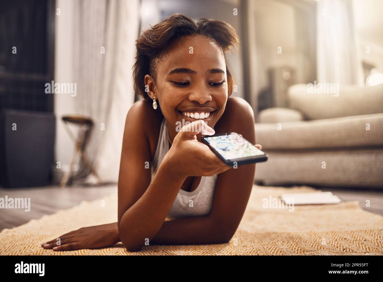 Una ragazza che invia SMS, chatta e naviga sui social media sul suo telefono mentre si rilassa a casa. Giovane donna alla ricerca di un'app online, che si diverte con un'app sul pavimento del salotto Foto Stock