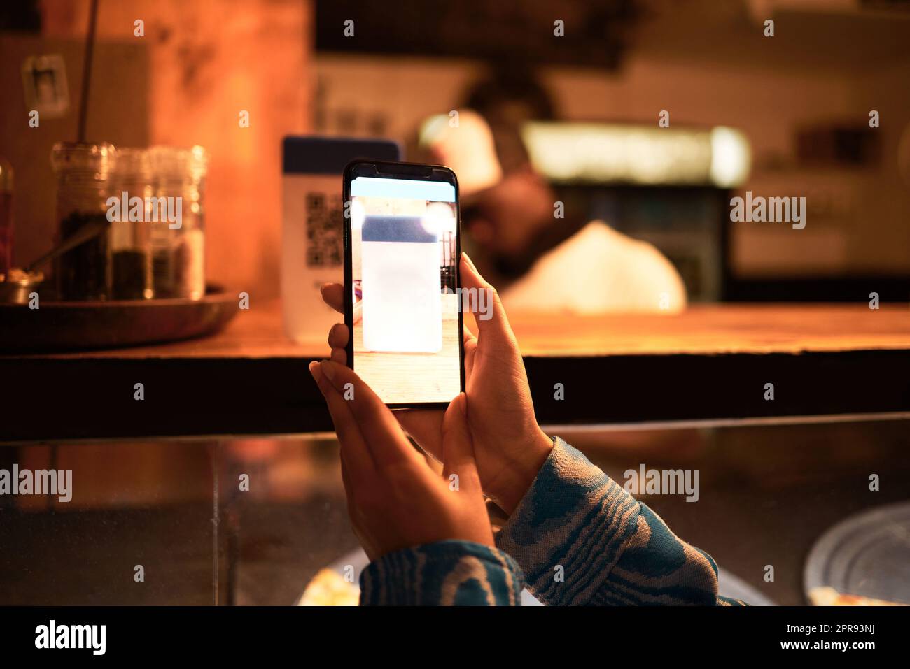 Persona con fotocamera del telefono che scansiona il codice a barre QR per il menu online in un moderno ristorante, negozio o caffetteria di sera. Mano di una donna che fa una scansione fotografica per ottenere informazioni sul sito Web utilizzando la tecnologia moderna Foto Stock