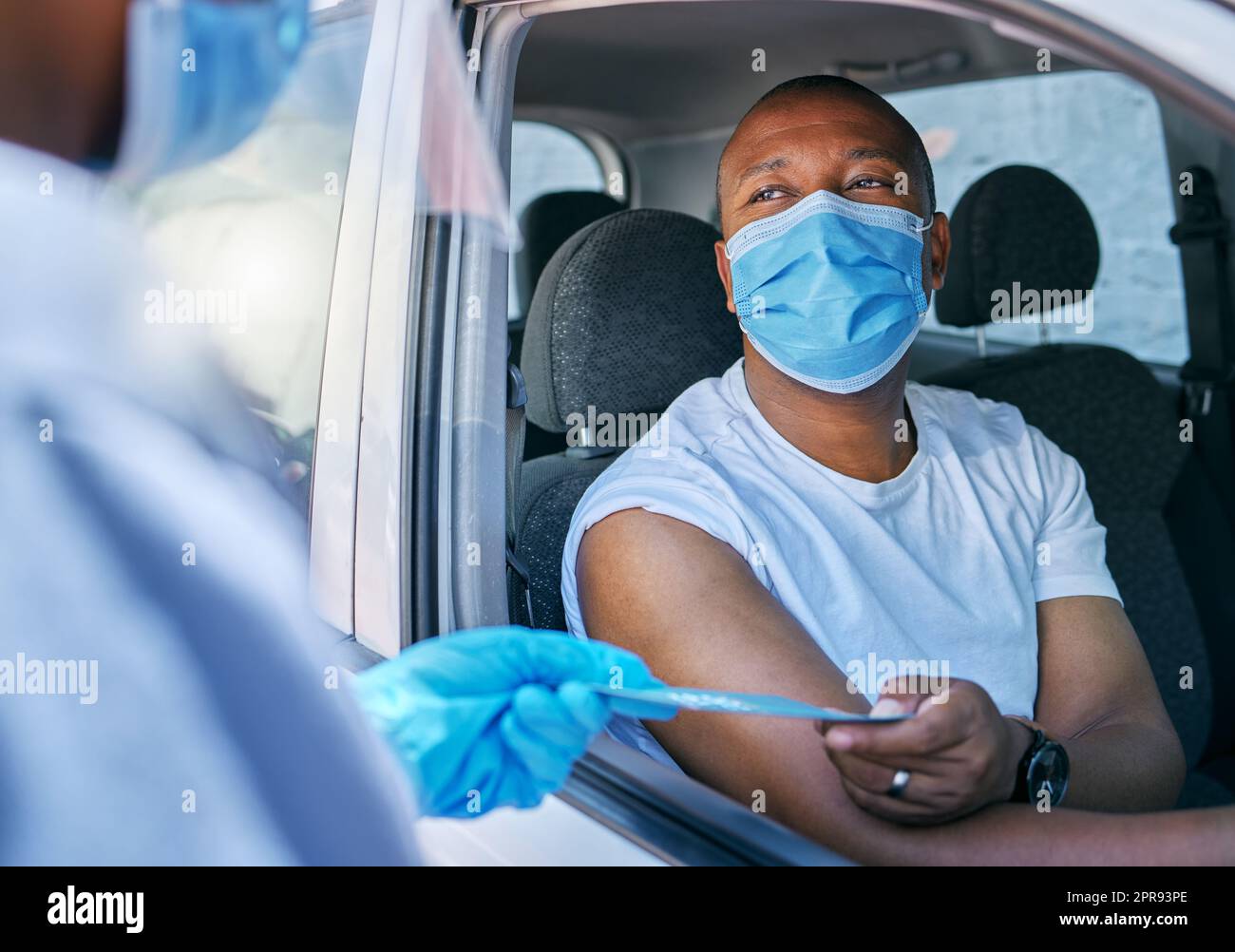 Guidare attraverso il servizio informazioni sul vaccino anti covid all'aperto per un paziente in auto. Un operatore sanitario che consegna un opuscolo a un uomo in un veicolo dopo il trattamento con coronavirus in una stazione di vaccinazione Foto Stock