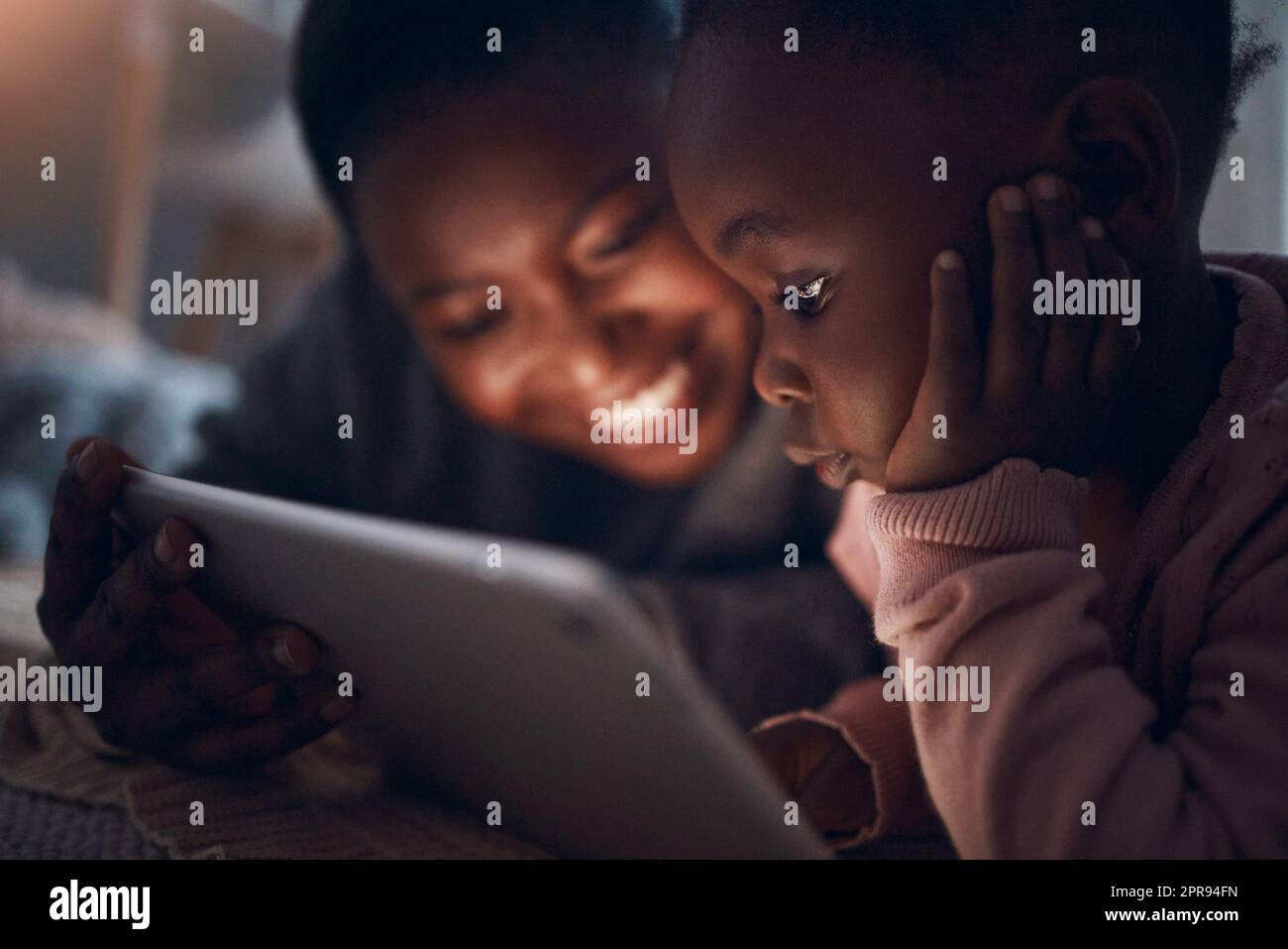 Cosa pensi che succederà dopo. Una madre che legge le storie dell'ora di dormire con sua figlia su un tablet digitale. Foto Stock