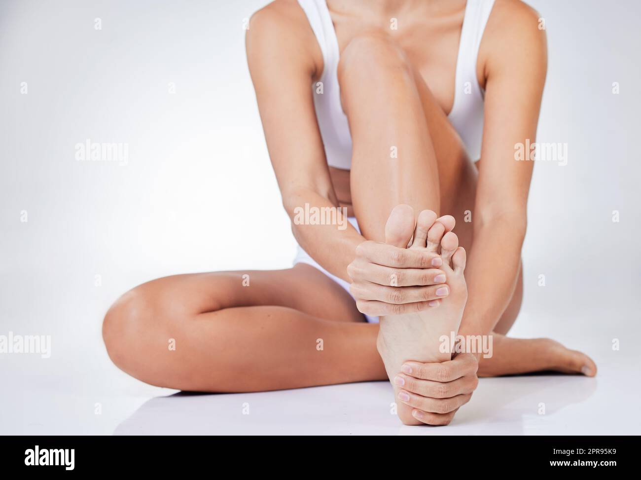 Prendermi cura dei miei piedi. Una donna seduta sul pavimento massaggiando il piede contro uno sfondo di studio. Foto Stock