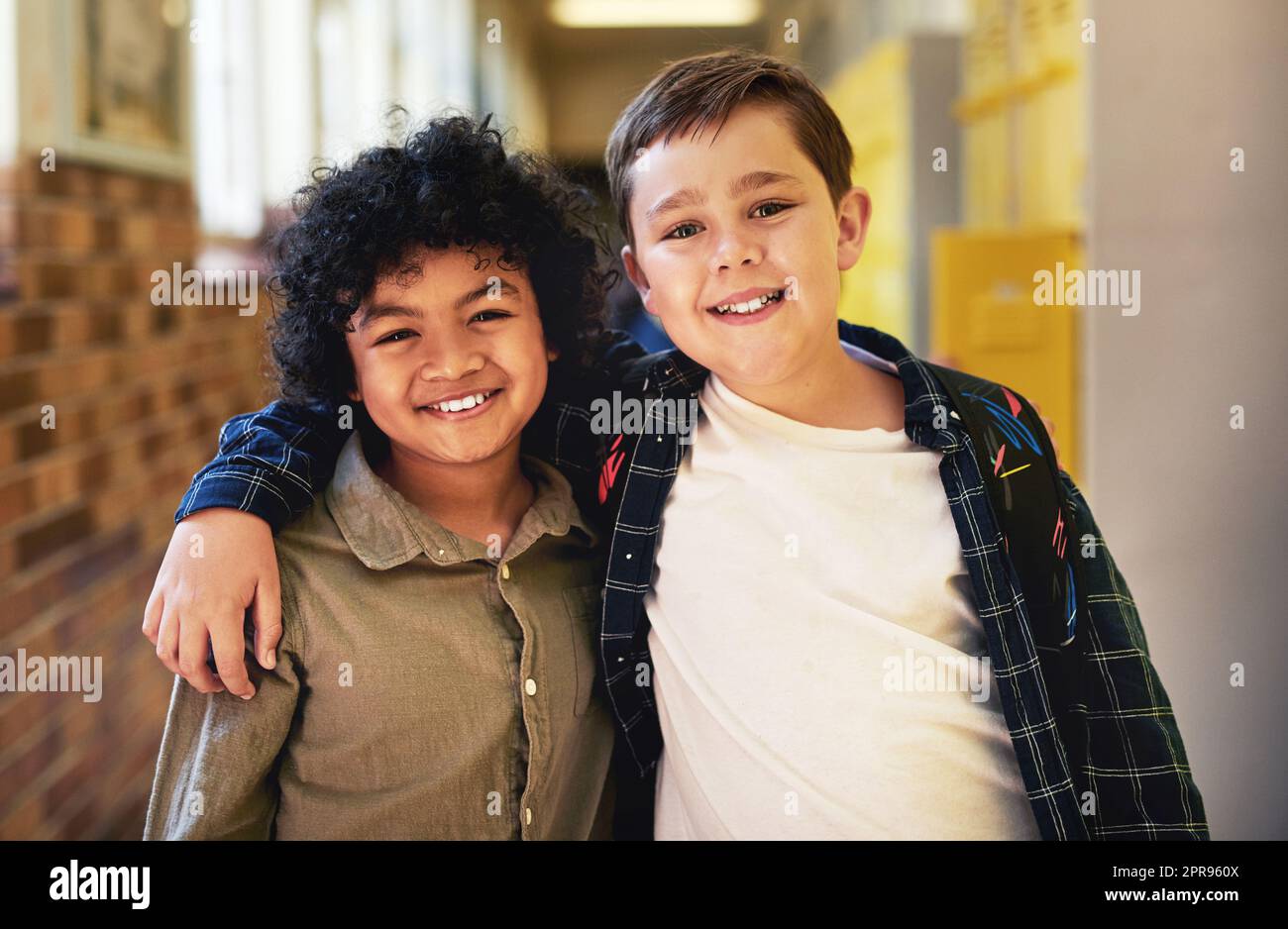 Gli amici sono la parte migliore della scuola: Due giovani ragazzi che si levano in piedi nel corridoio a scuola con le braccia l'uno intorno all'altro. Foto Stock