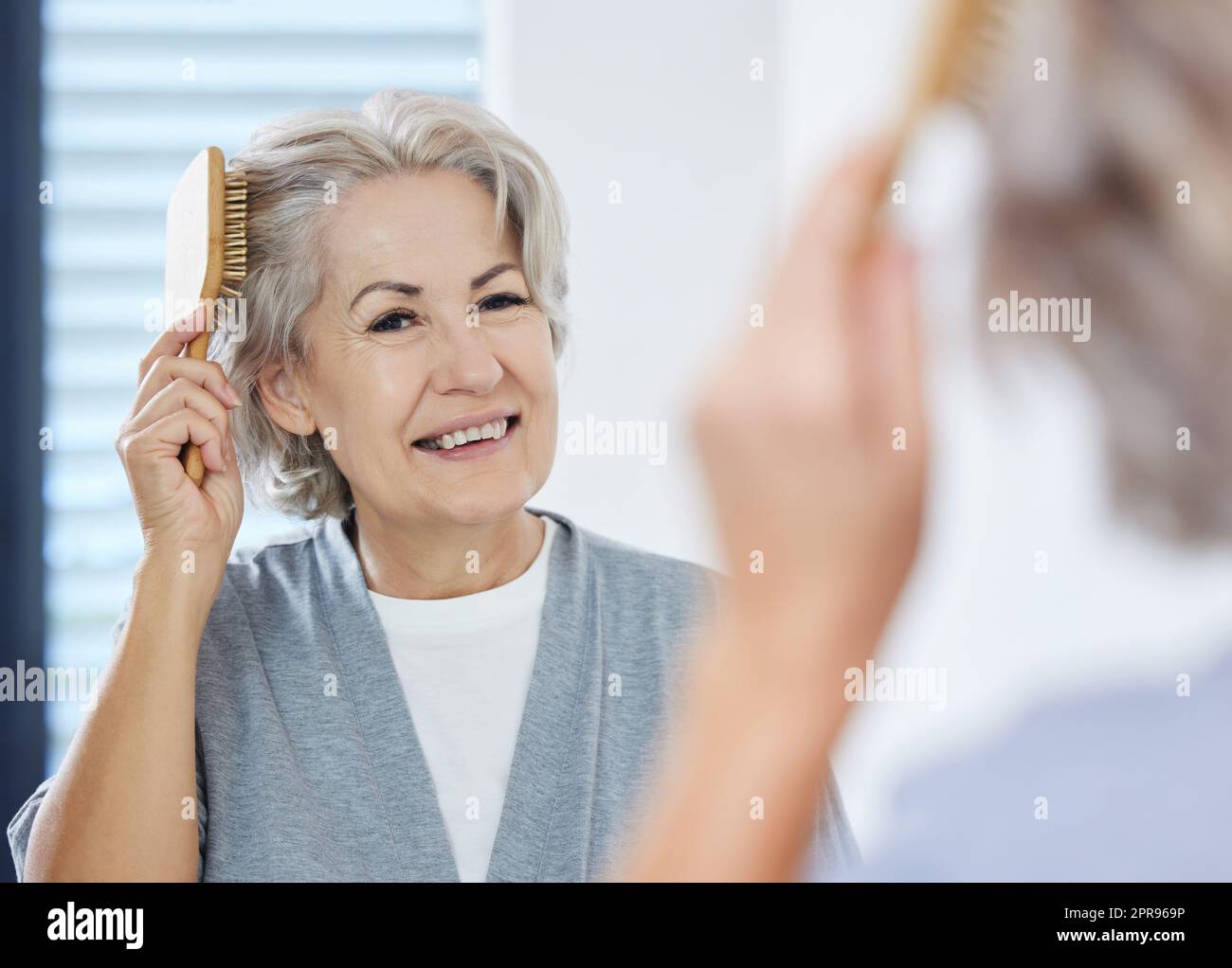 Gray Sure mi sembra buona, una donna anziana che le spazzolava i capelli guardando nello specchio del bagno. Foto Stock