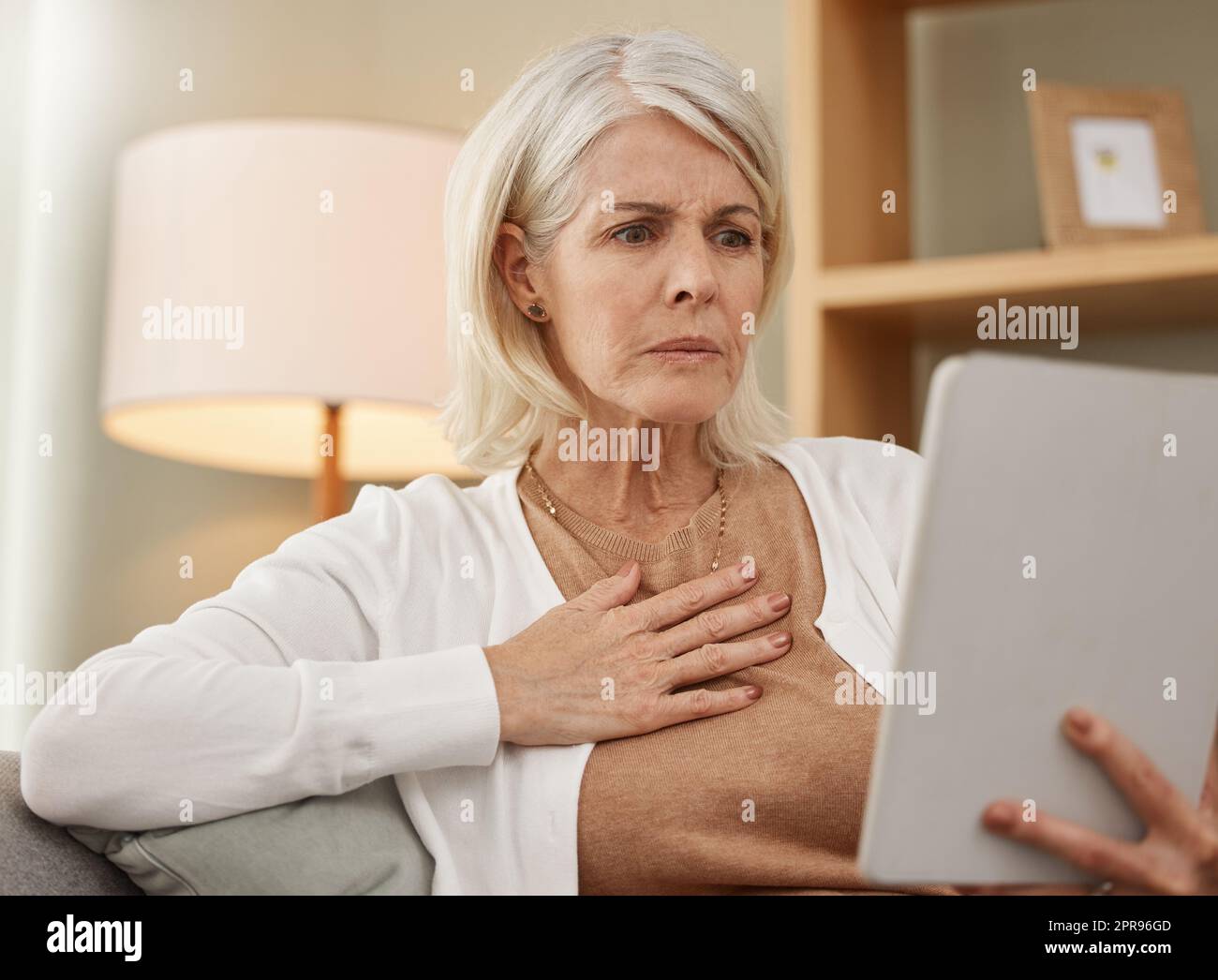 Forse dovrei fare un doppio controllo con il mio medico: Una donna matura che usa un tablet digitale e che guarda preoccupata a casa. Foto Stock