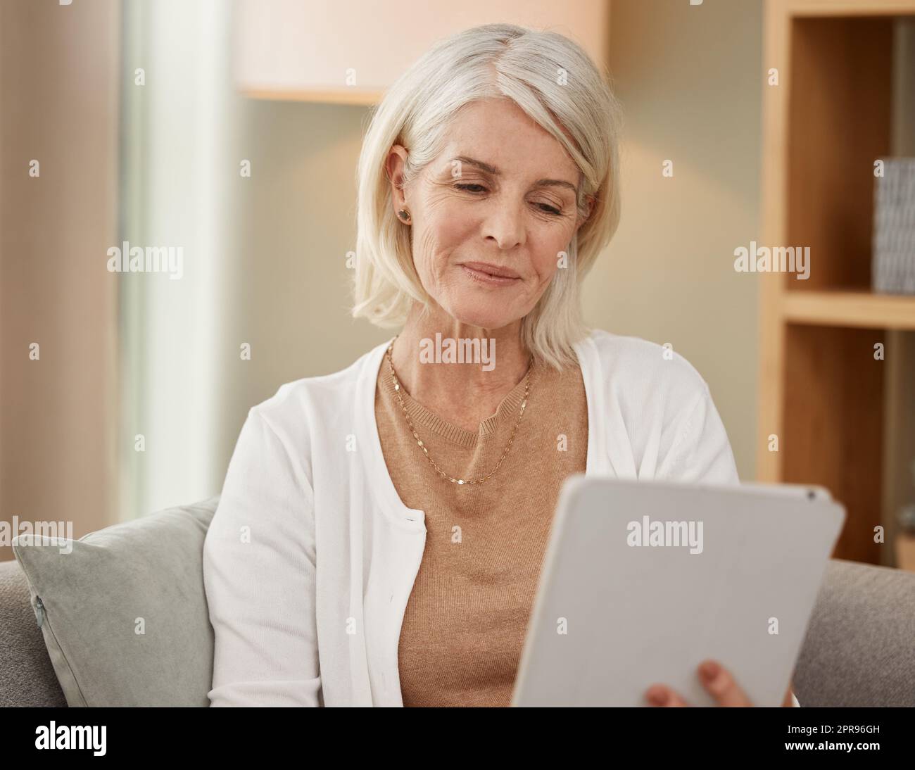 Bene, qualcosa che non ho mai conosciuto: Una donna matura che usa un tablet digitale sul divano di casa. Foto Stock