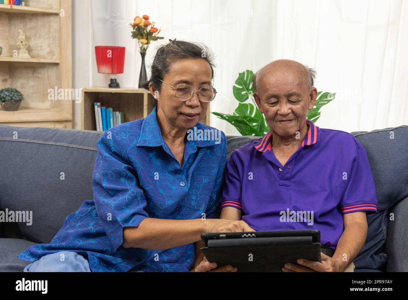 Senior asiatici che utilizzano la tecnologia di comunicazione Internet online tablet sul divano a casa. Foto Stock