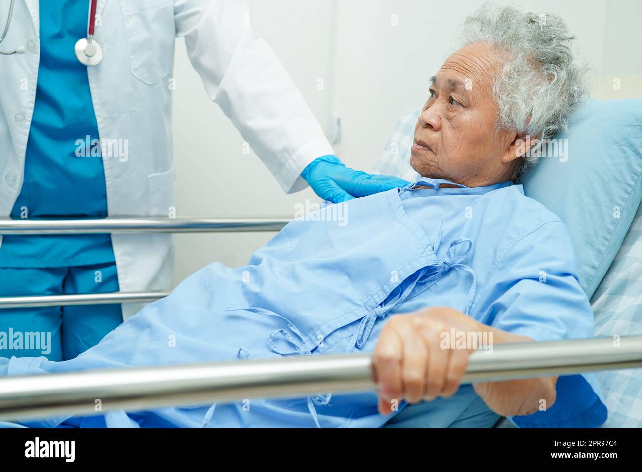 Donna anziana asiatica che tiene la barra del letto mentre si sdraia con speranza in attesa della sua famiglia in ospedale. Foto Stock