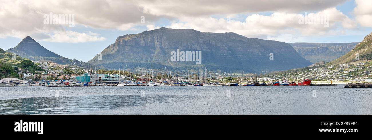 Splendida vista dell'oceano e del cielo azzurro nuvoloso con Table Mountain sullo sfondo. Tranquillo paesaggio marino con spazi fotografici ed edifici urbani vicino al porto di città del Capo, in Sudafrica Foto Stock