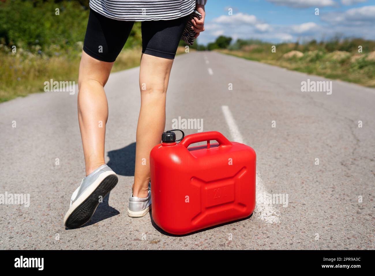 Un'auto parcheggiata sul lato della strada, un contenitore rosso vuoto. La ragazza si ferma sulla strada per riempire la macchina. Mancanza di carburante - olio, diesel, benzina. Foto Stock