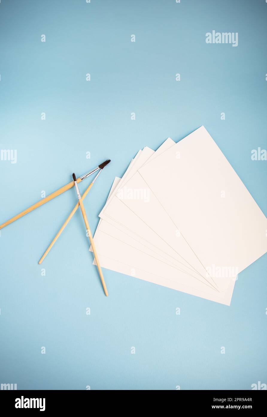 Pennelli ad acquerello di dimensioni diverse si trovano insieme alla carta ad acquerello su sfondo blu. Lezioni di disegno. Foto Stock