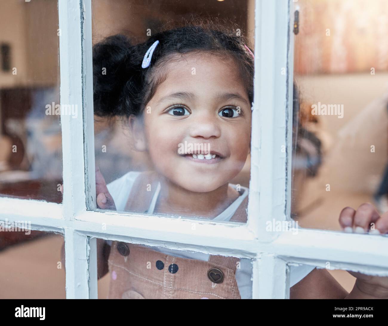 Lasciatemi fuori, una bambina adorabile che guarda attraverso la finestra a casa. Foto Stock