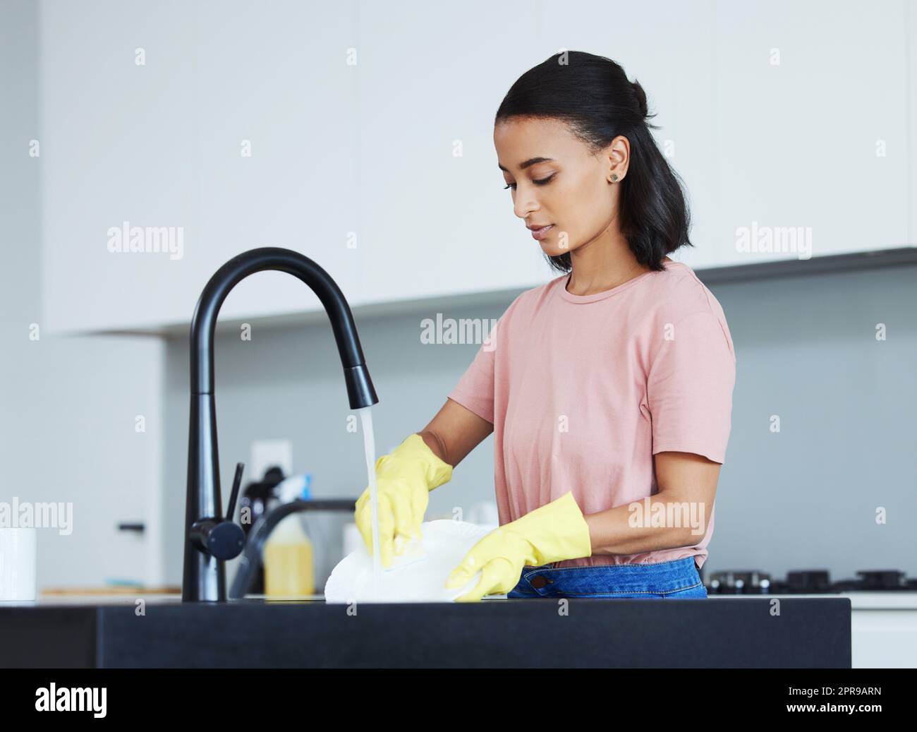 Fare i piatti non è mai divertente. Una giovane donna che lava i piatti in cucina. Foto Stock