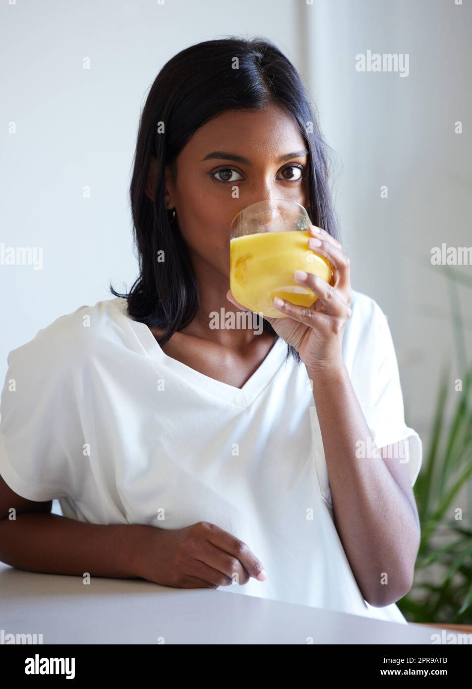 Sarà una giornata fruttuosa, una bella giovane donna che beve un bicchiere di succo d'arancia a casa. Foto Stock